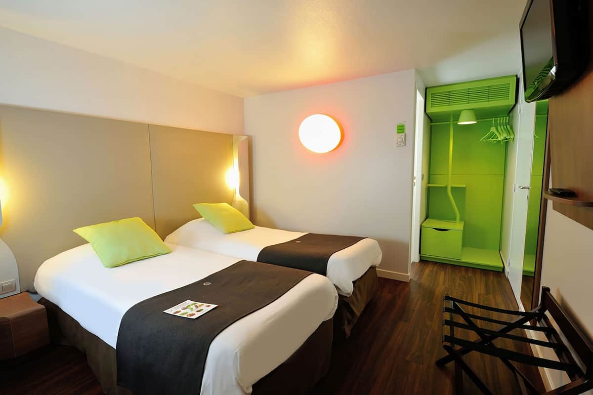 A hotel room with two beds, a green closet, and a round wall light.