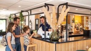 A reception area with a counter, a staff member, and a family interacting. - Hotel Campanile Saint Etienne Centre - Villars (Villars)