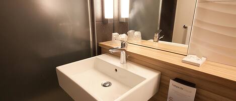 A modern bathroom with a white sink, a mirror, and a wooden countertop.