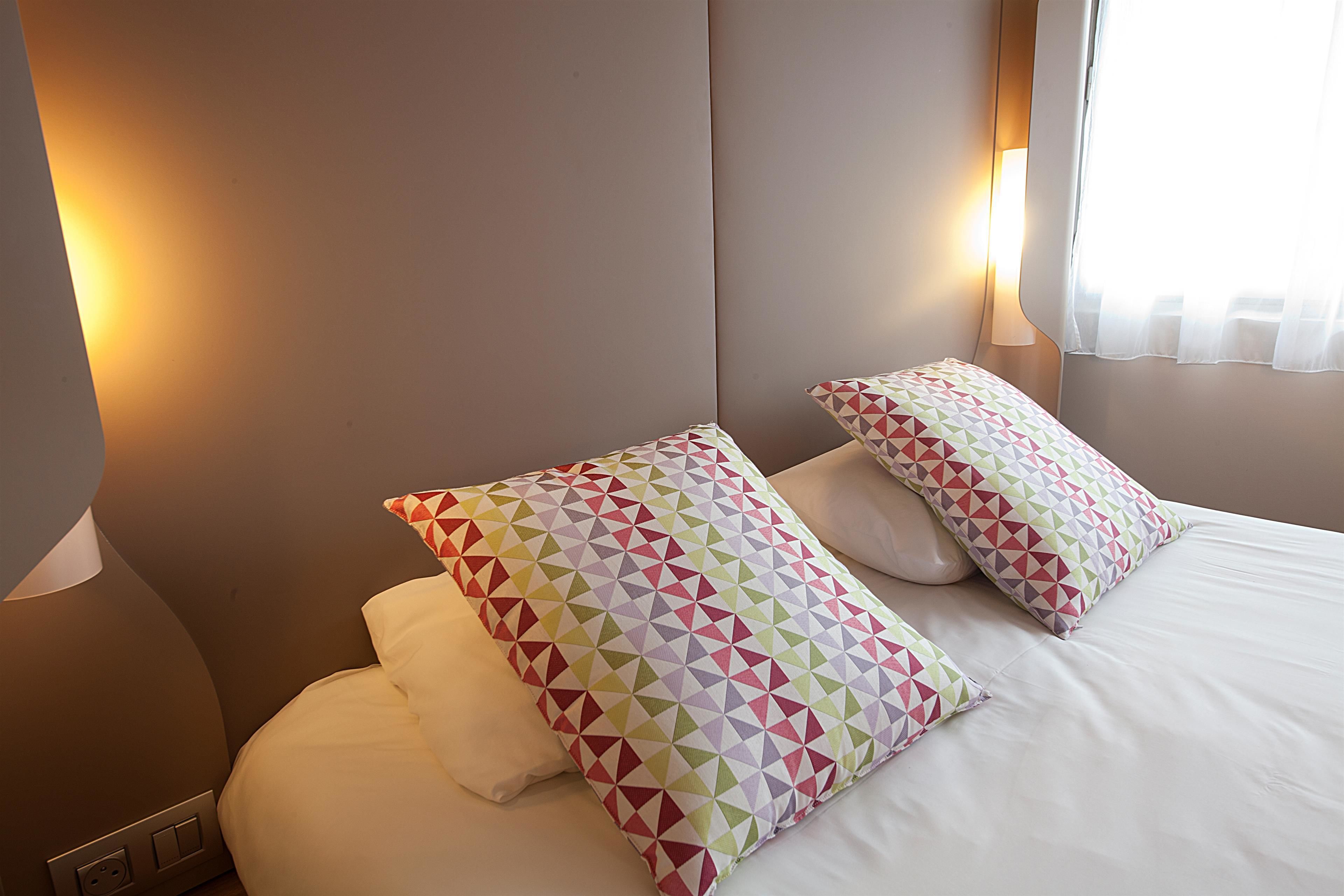A neatly made bed with patterned pillows and a bedside lamp.