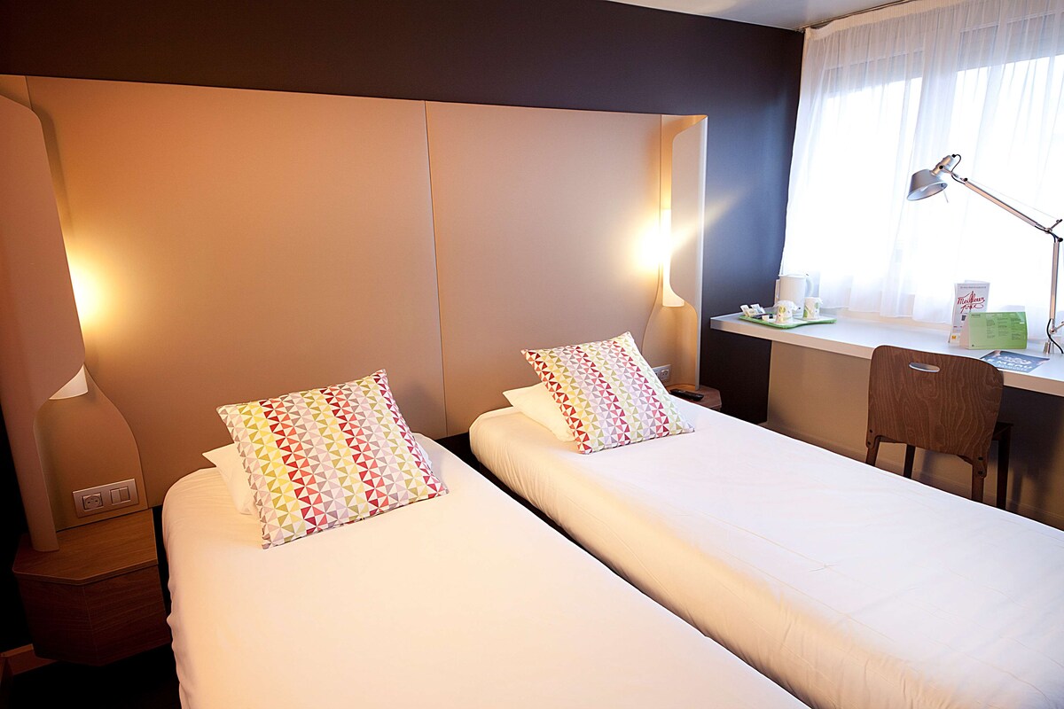 Une chambre d’hôtel avec deux lits, un bureau, une chaise et une lampe.