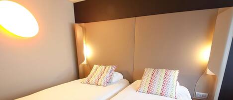 Ein Hotelzimmer mit Bett, zwei Kissen, Wandlampe und Steckdose.