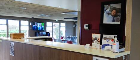 A reception desk with a wooden counter, a television screen displaying a program, and a sign with information for guests.