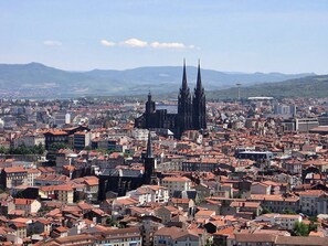 Eine Stadtansicht mit einem markanten Dom, der mit zwei Türmen verziert ist, umgeben von dicht bebauten Gebäuden mit roten Ziegeldächern.
