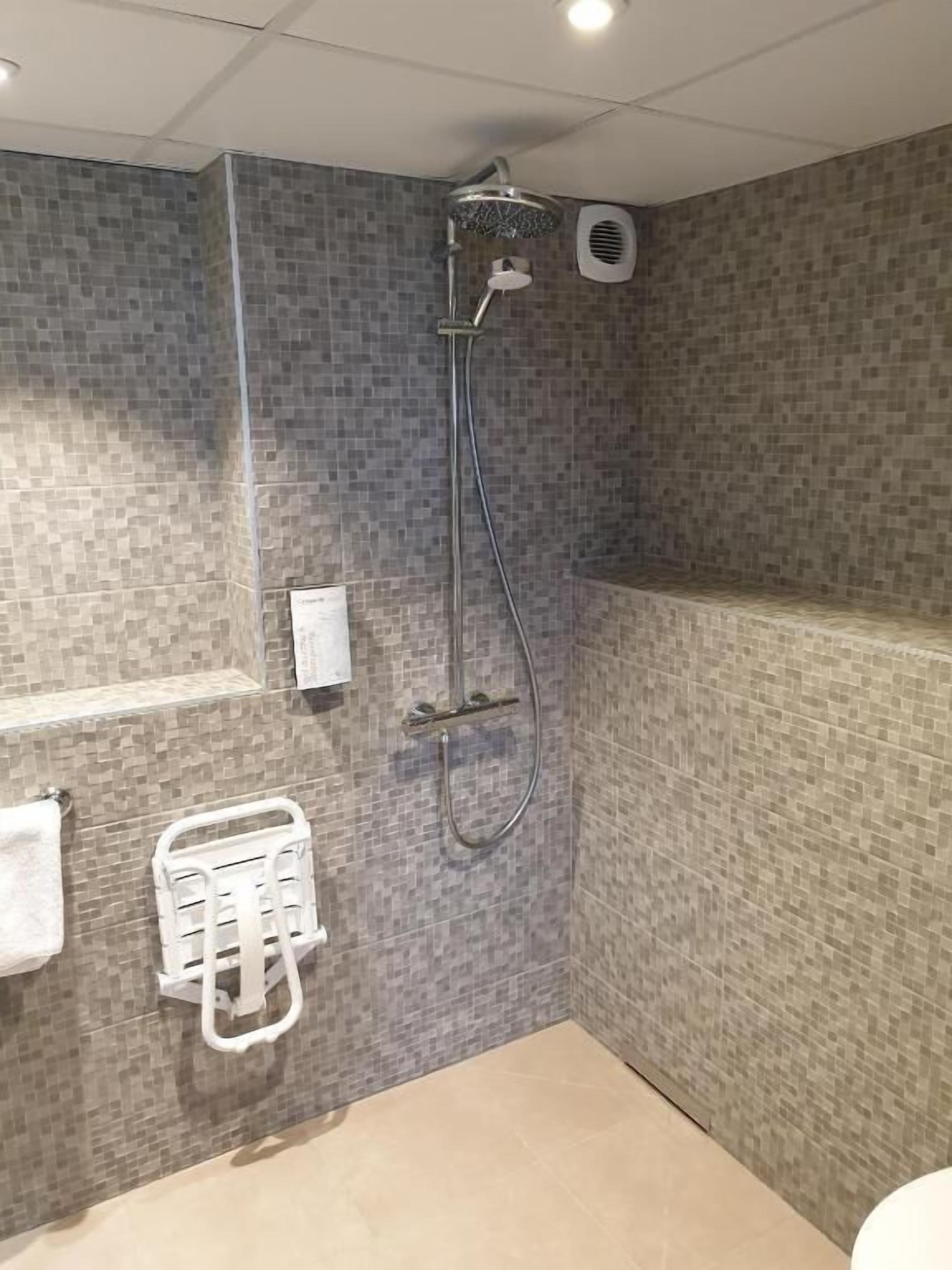 A bathroom with a shower, tiled walls, a towel rack, and a hand dryer.