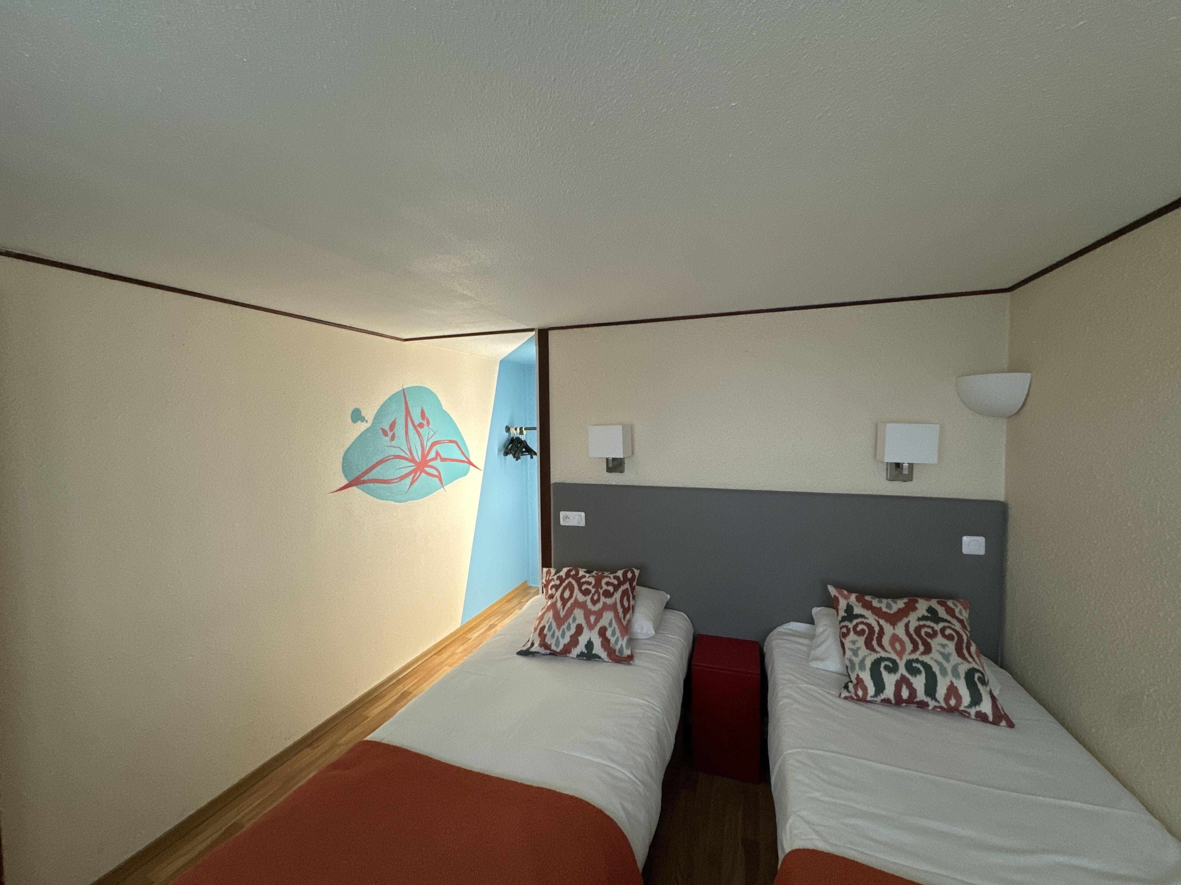 A hotel room with two beds, a red accent wall, and a decorative wall art piece.