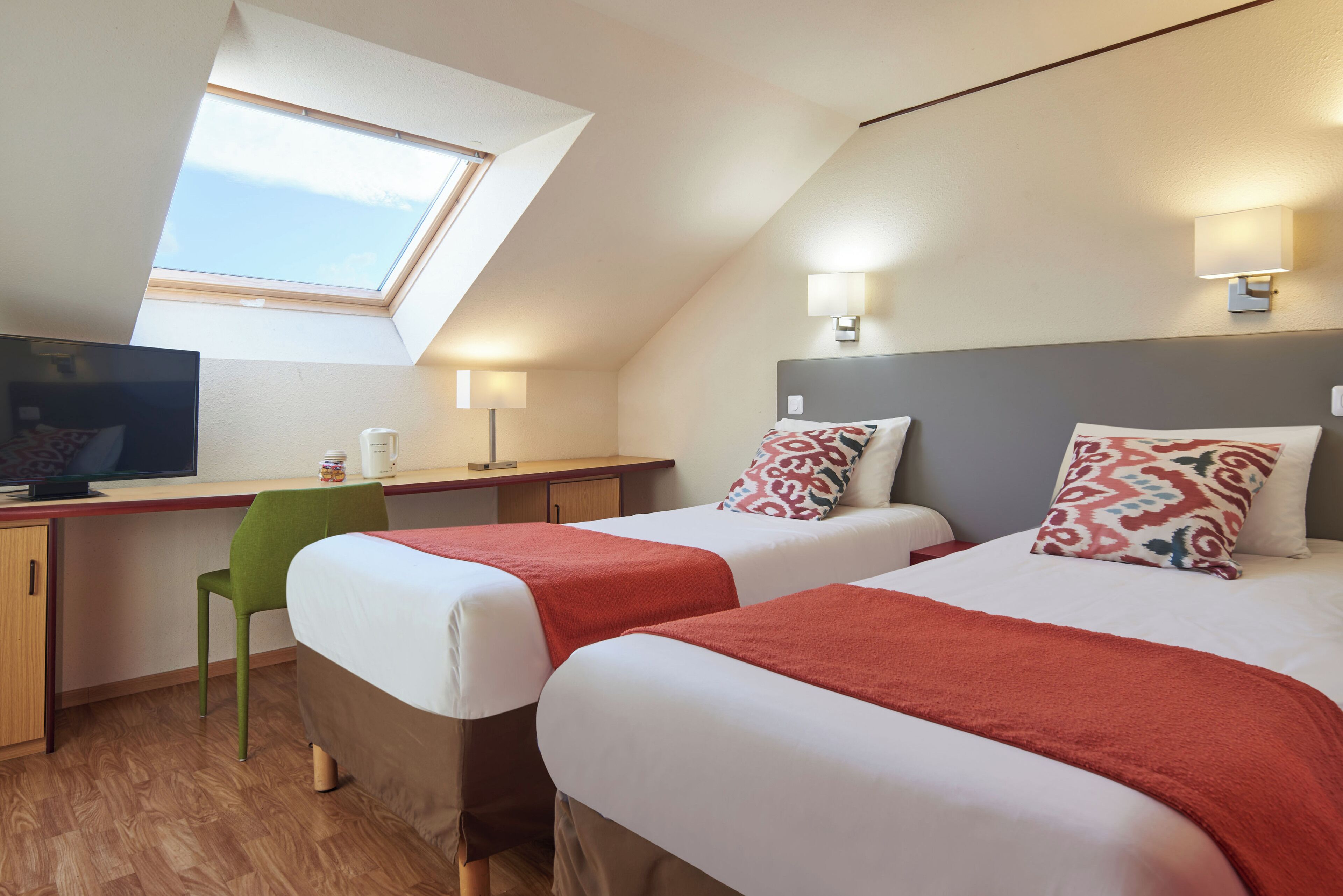 A room with two beds, a desk, a chair, a TV, and a skylight.