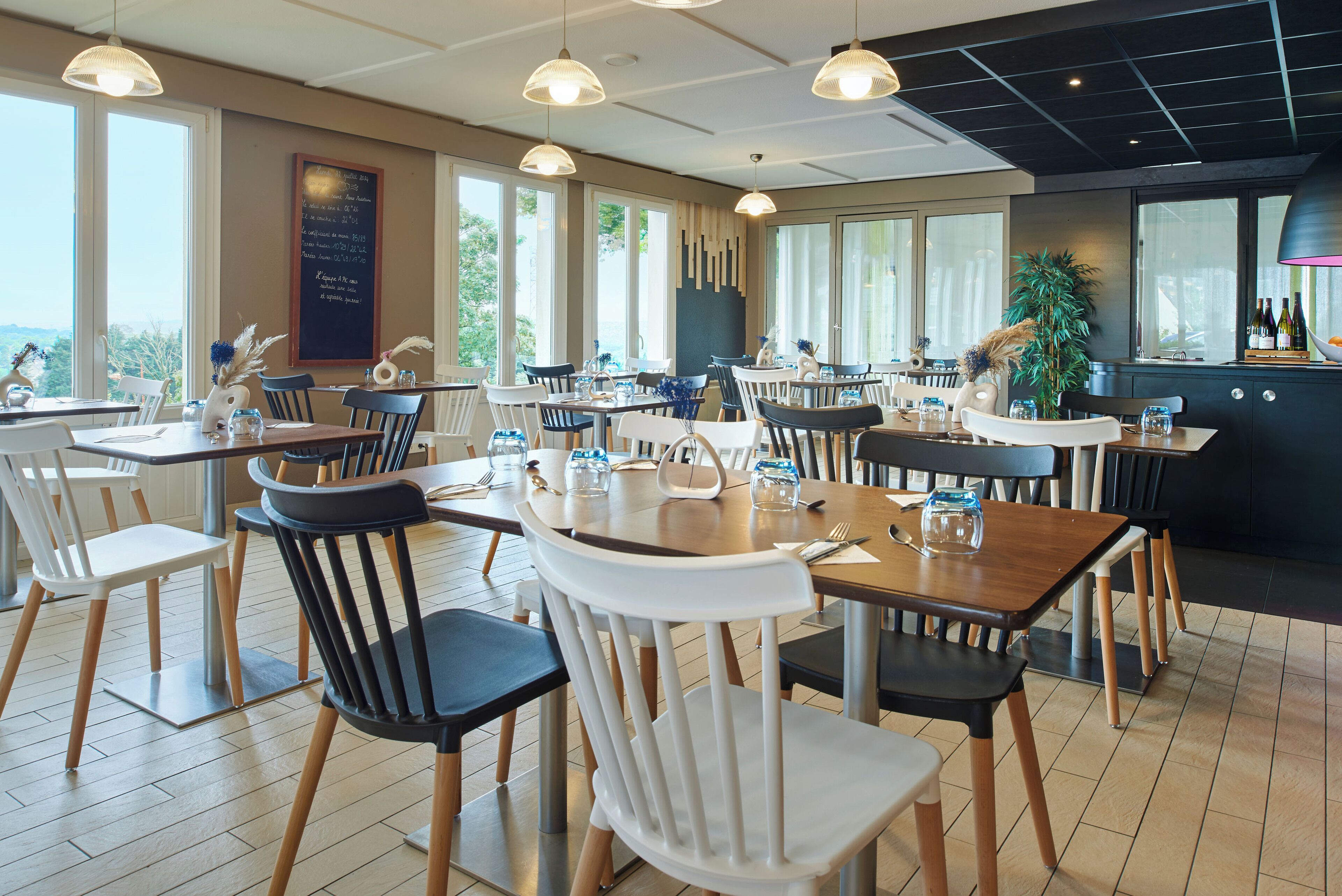 A restaurant with multiple tables and chairs, large windows, and a view of the outdoors.