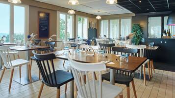 A restaurant with multiple tables and chairs, large windows, and a view of the outdoors.