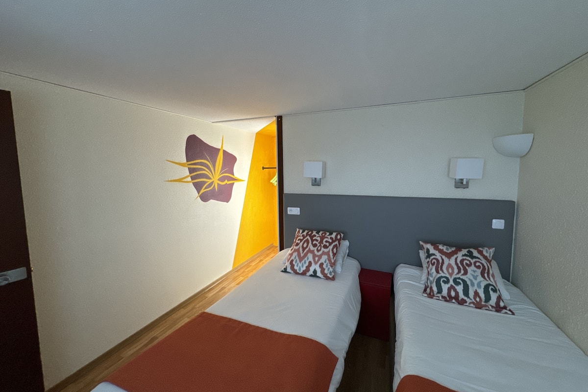 Quarto de hotel com duas camas, uma luminária na parede e uma peça de arte original.