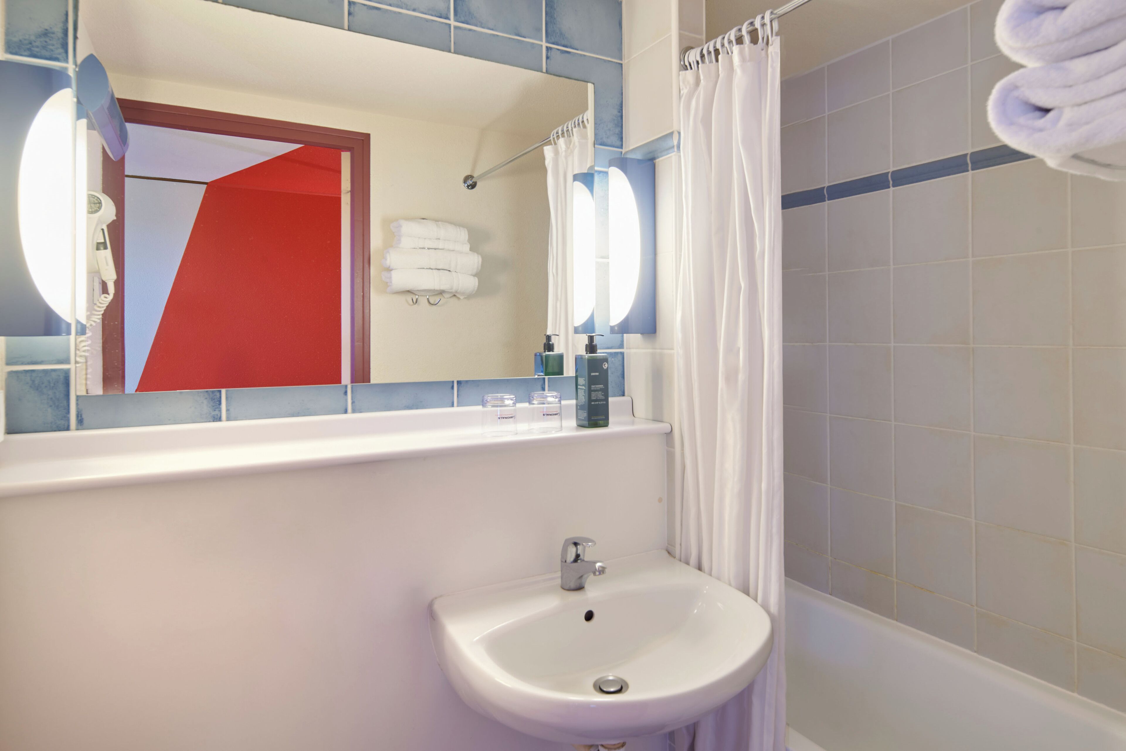 Une salle de bain avec un lavabo blanc, un miroir et un rideau de douche.