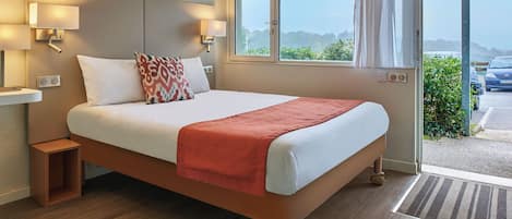 Habitación de hotel con una cama grande, dos lámparas de noche, un ventanal con cortinas y vistas al exterior.