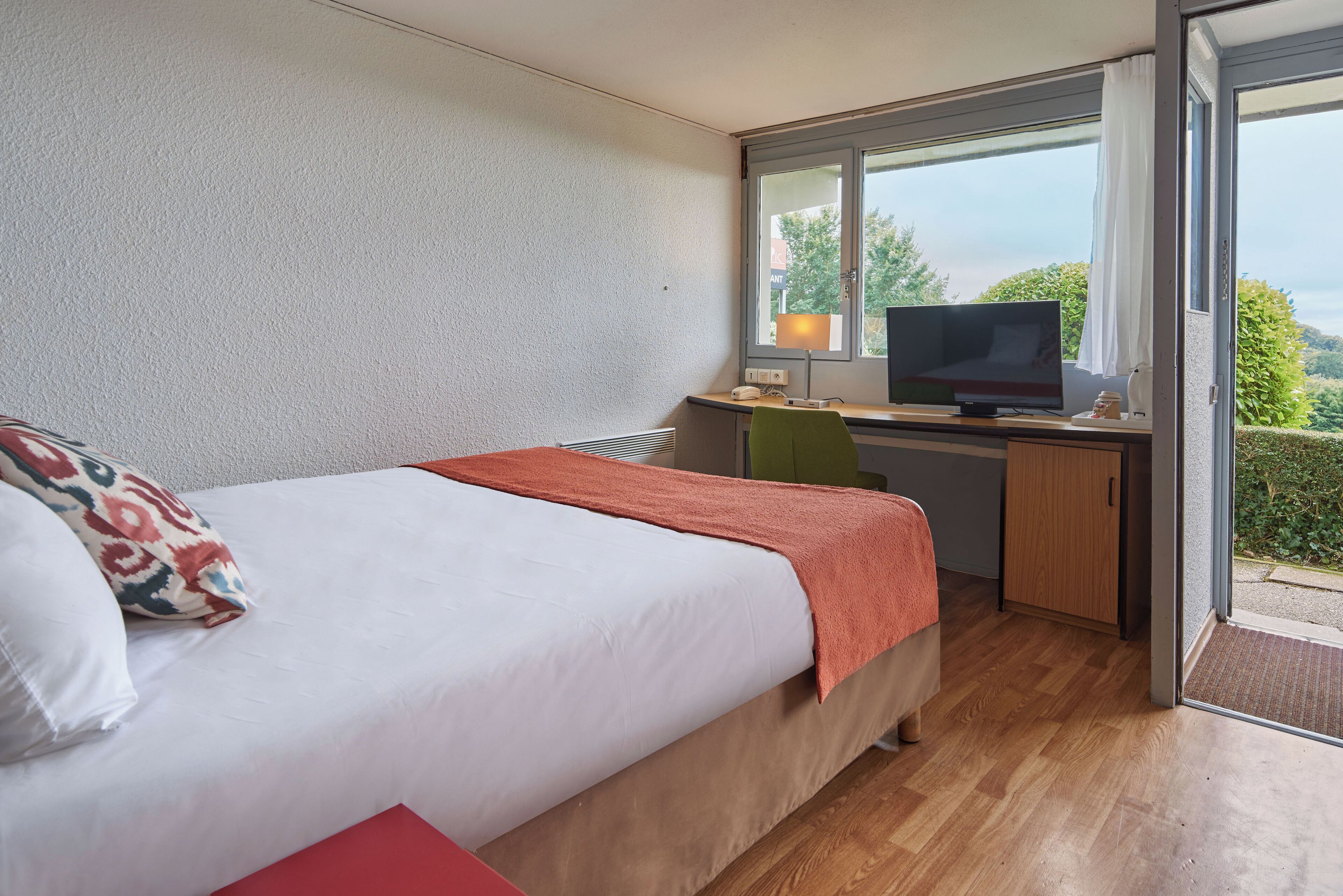 Una camera da letto con un letto, una scrivania con un computer e una finestra vista verde.