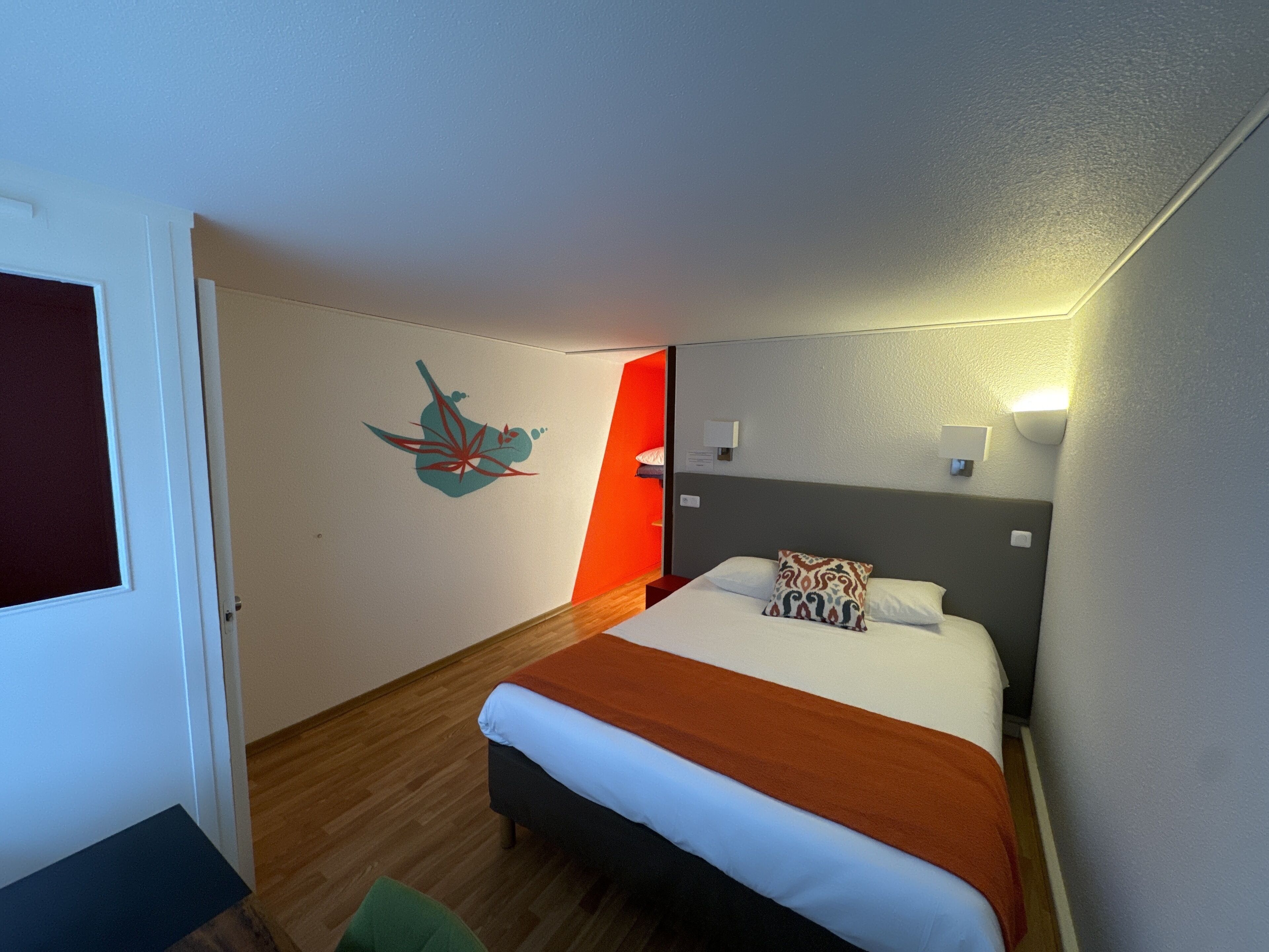 Una habitación de hotel con una cama, una obra de arte en la pared, una mesita de noche y otra mesita auxiliar.