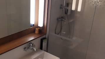 Un baño con ducha envuelta en vidrio, un lavabo con espejo y un inodoro.