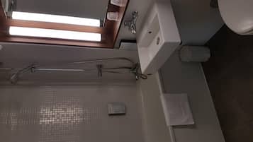 A bathroom with a shower, sink, and toilet. There is a window above the shower, and a towel is hanging on the wall.