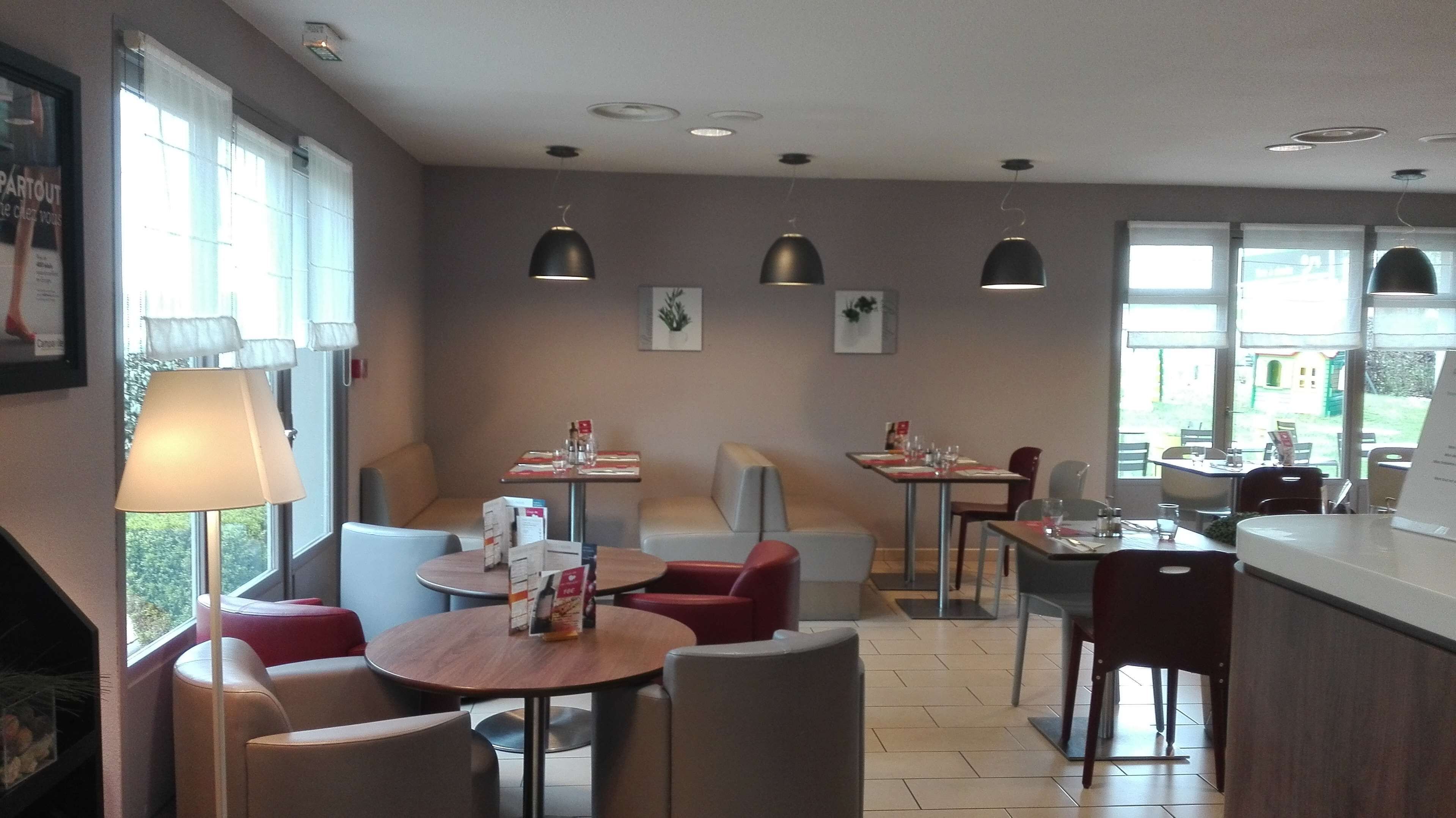 Ein Restaurant mit runden Tischen, roten und grauen Stühlen, Pendelleuchten und gerahmten Bildern an den Wänden.