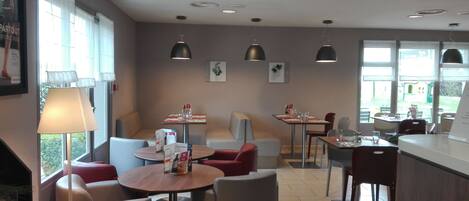 A restaurant with round tables, red and grey chairs, pendant lights, and framed pictures on the walls.