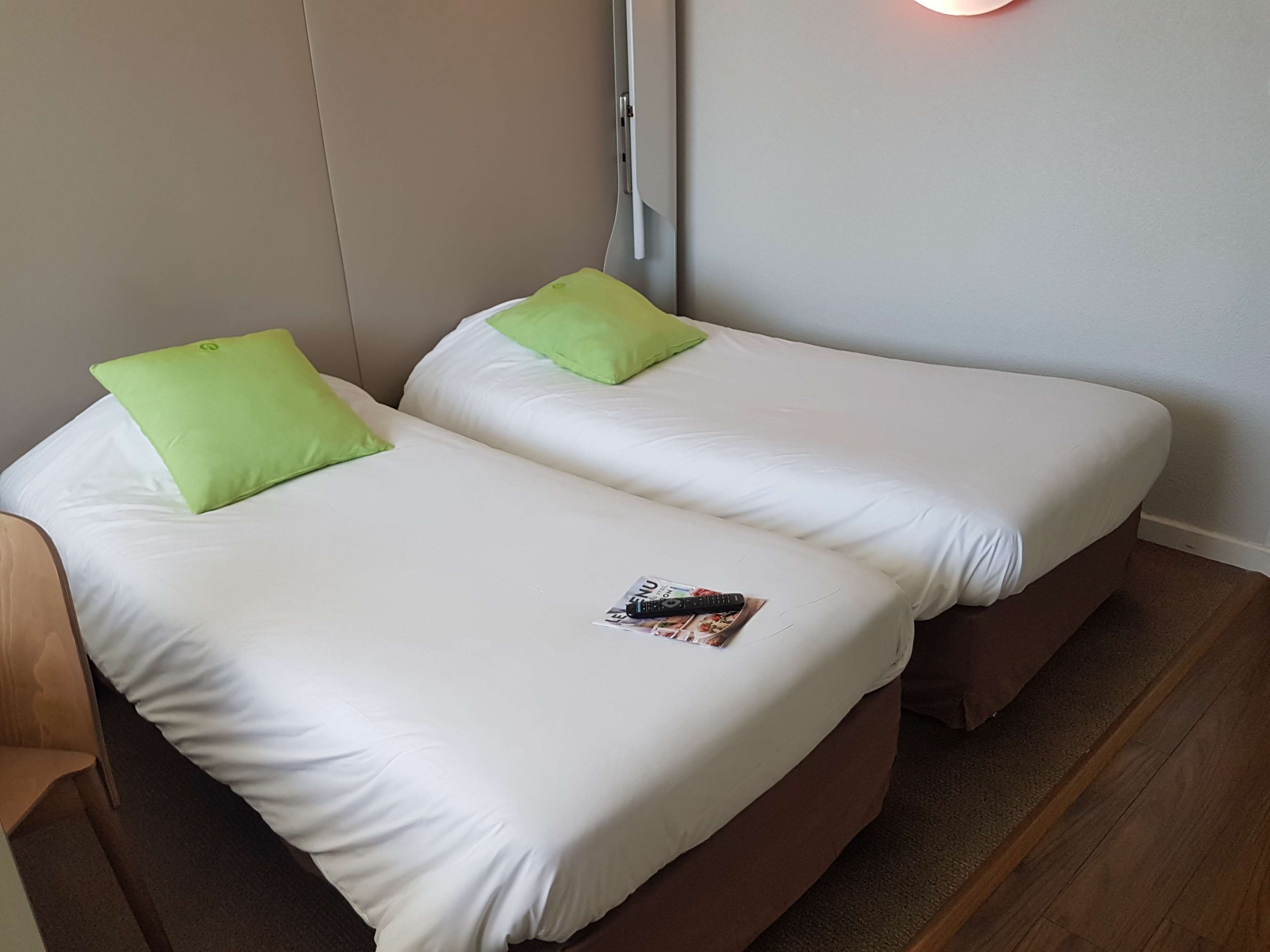 Une chambre double avec deux lits, chacun étant équipé de draps blancs et d’oreillers verts.
