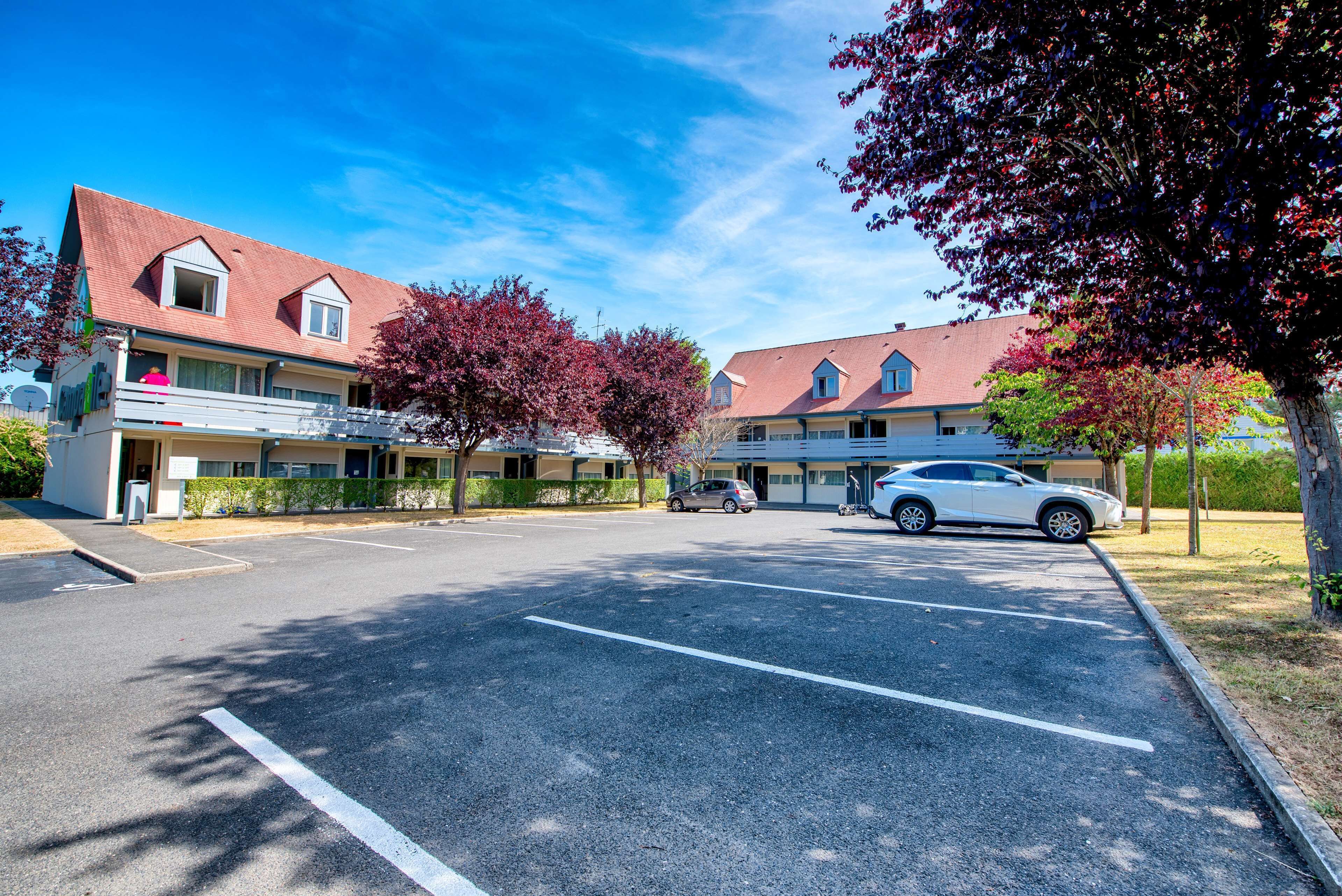 A hotel with a parking lot, a red-roofed building, and trees with pink leaves.