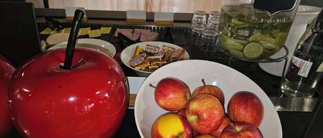 Una encimera de cocina con una manzana roja, un bol de manzanas, un tarro de pepinillos, una botella de agua y un plato de bombones.
