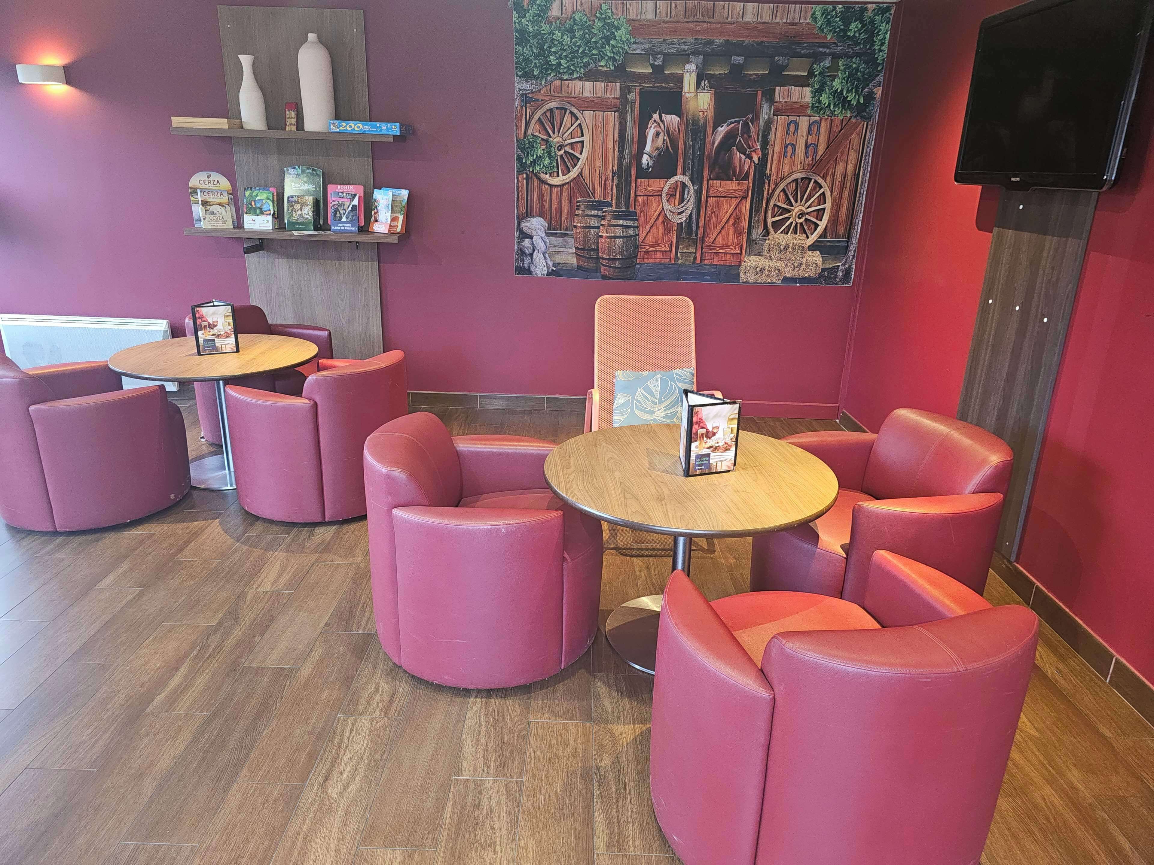 A restaurant interior with round tables and pink cushioned chairs, a wooden floor, and a wall-mounted TV.