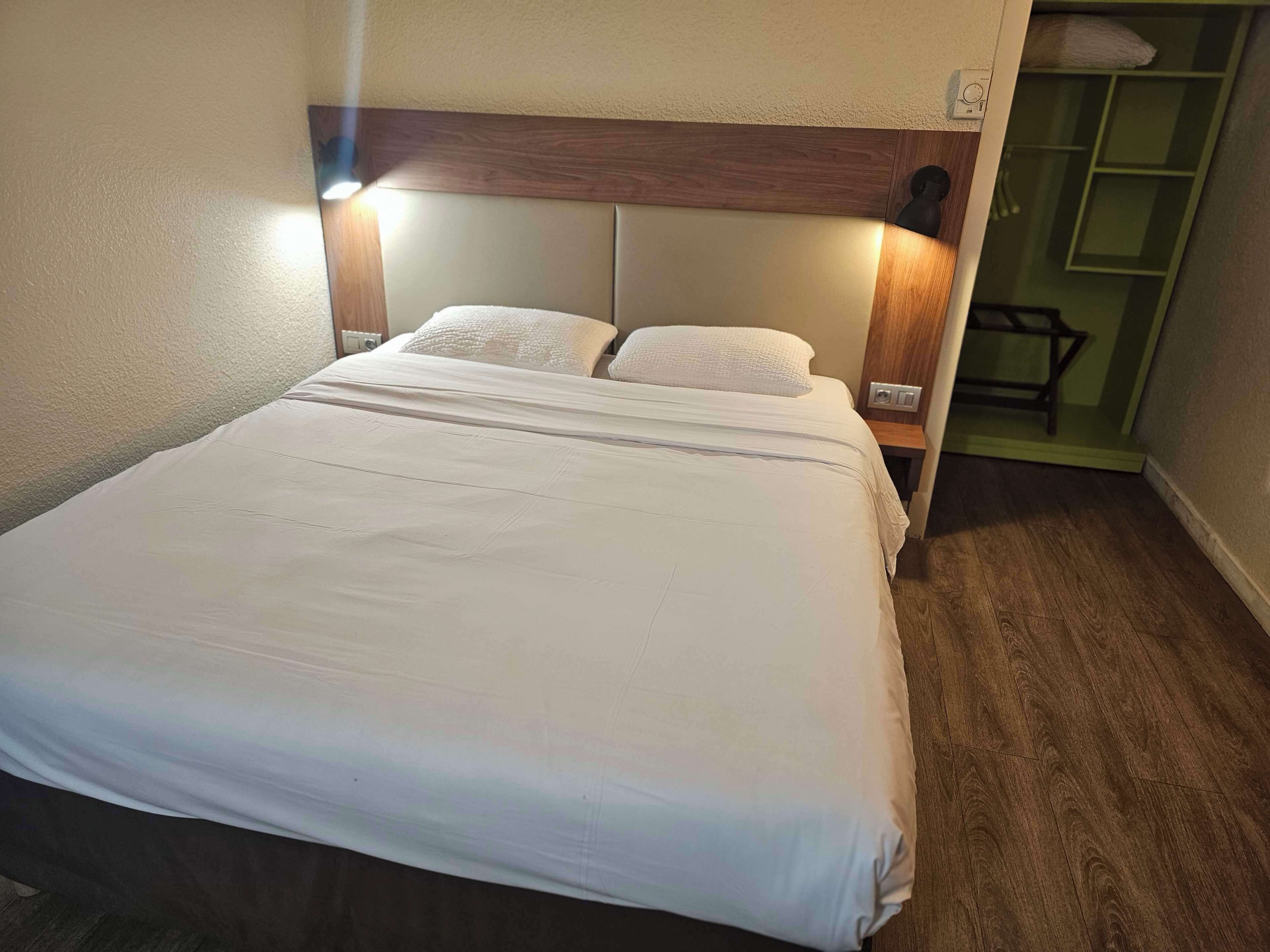 A neatly made bed with a wooden headboard, two bedside tables with lamps, and a green shelving unit in the background.