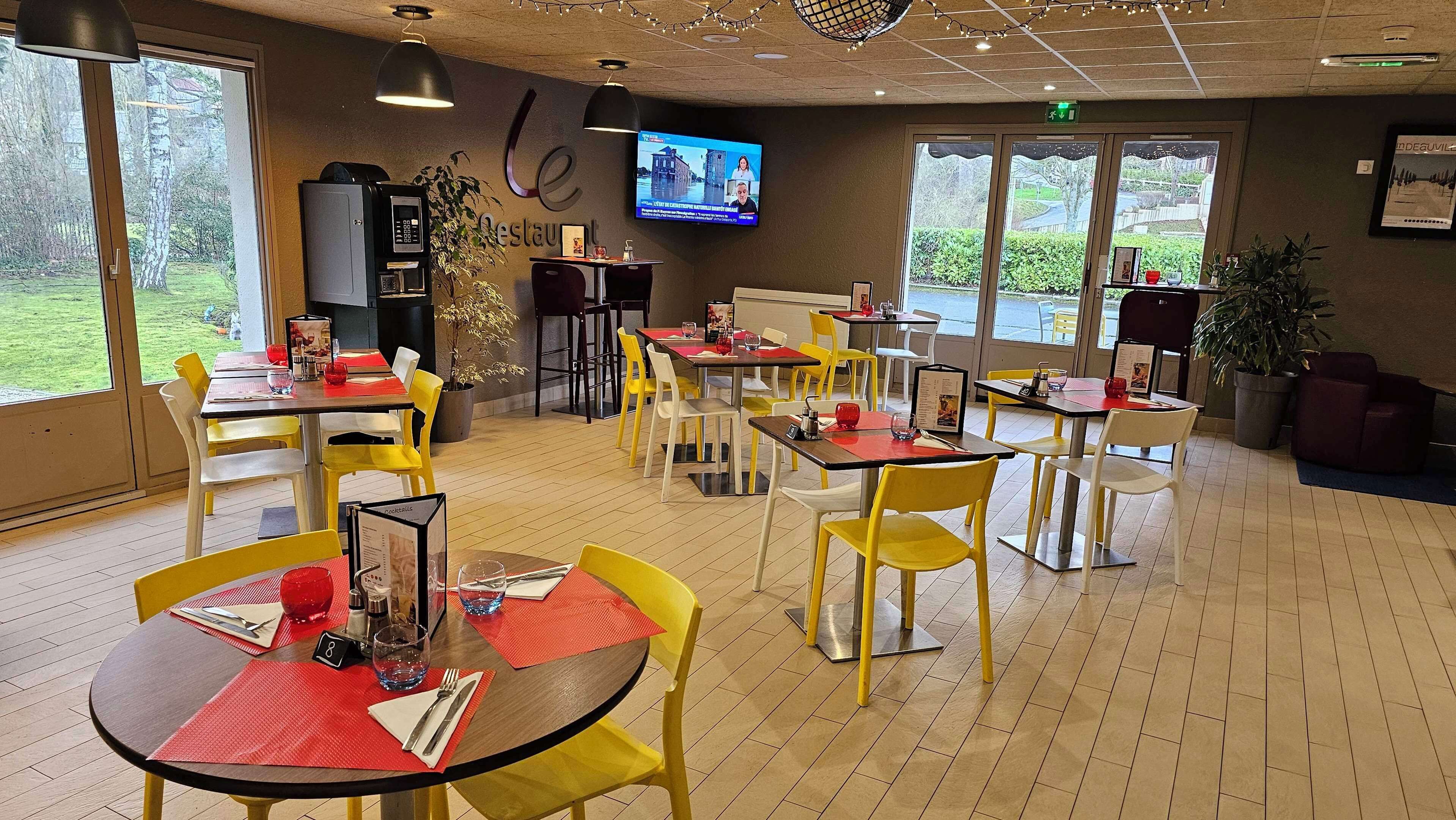 A restaurant with yellow and white chairs, red placemats, and a TV on the wall.