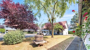 A landscaped area with a wooden barrel, a small bush, and a tree with red leaves. - Campanile Deauville St Arnoult (Saint-Arnoult)