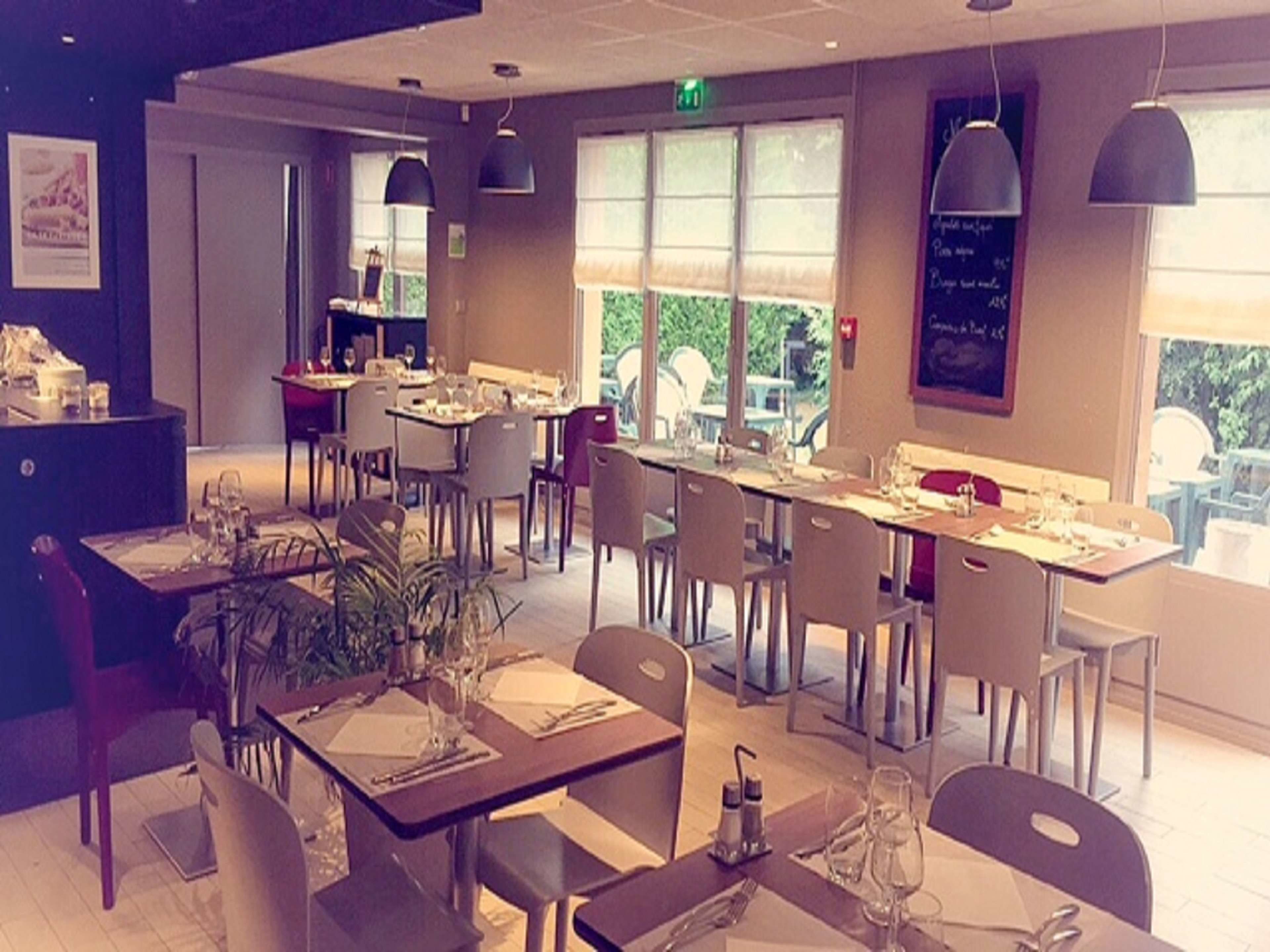 Un restaurante con varias mesas y sillas, ventanas amplias e iluminación colgante.
