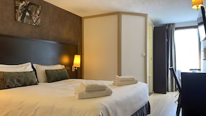 A hotel room with a large bed, two bedside lamps, a painting on the wall, and a view of the outside through the window.