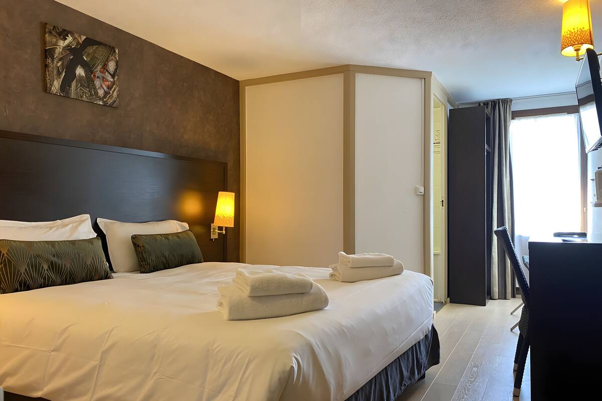 Ein Hotelzimmer mit einem großen Bett, zwei Nachttischlampen, einem Bild an der Wand und Blick aus dem Fenster.