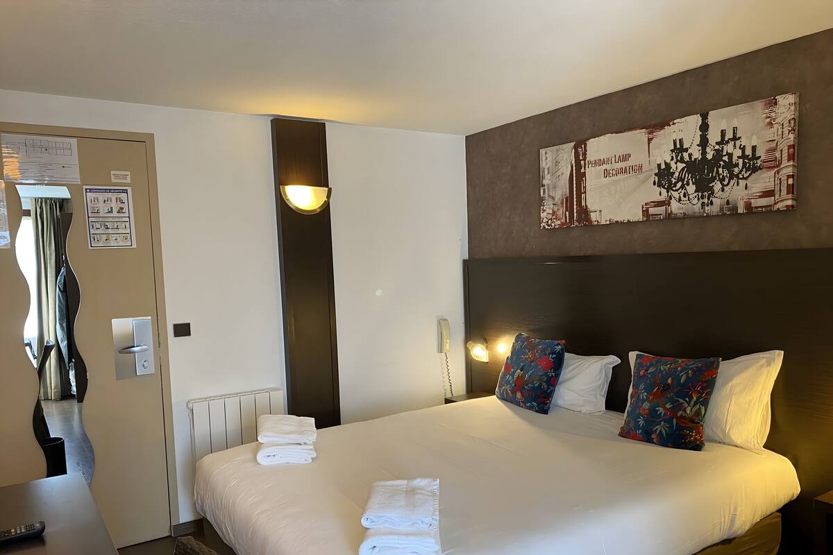 Ein Hotelzimmer mit einem großen Bett, zwei Kissen, einem Nachttisch, einer Lampe und einem Gemälde an der Wand.