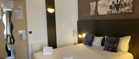 Une chambre d’hôtel avec un grand lit, deux oreillers, une table de chevet, une lampe et un tableau au mur.