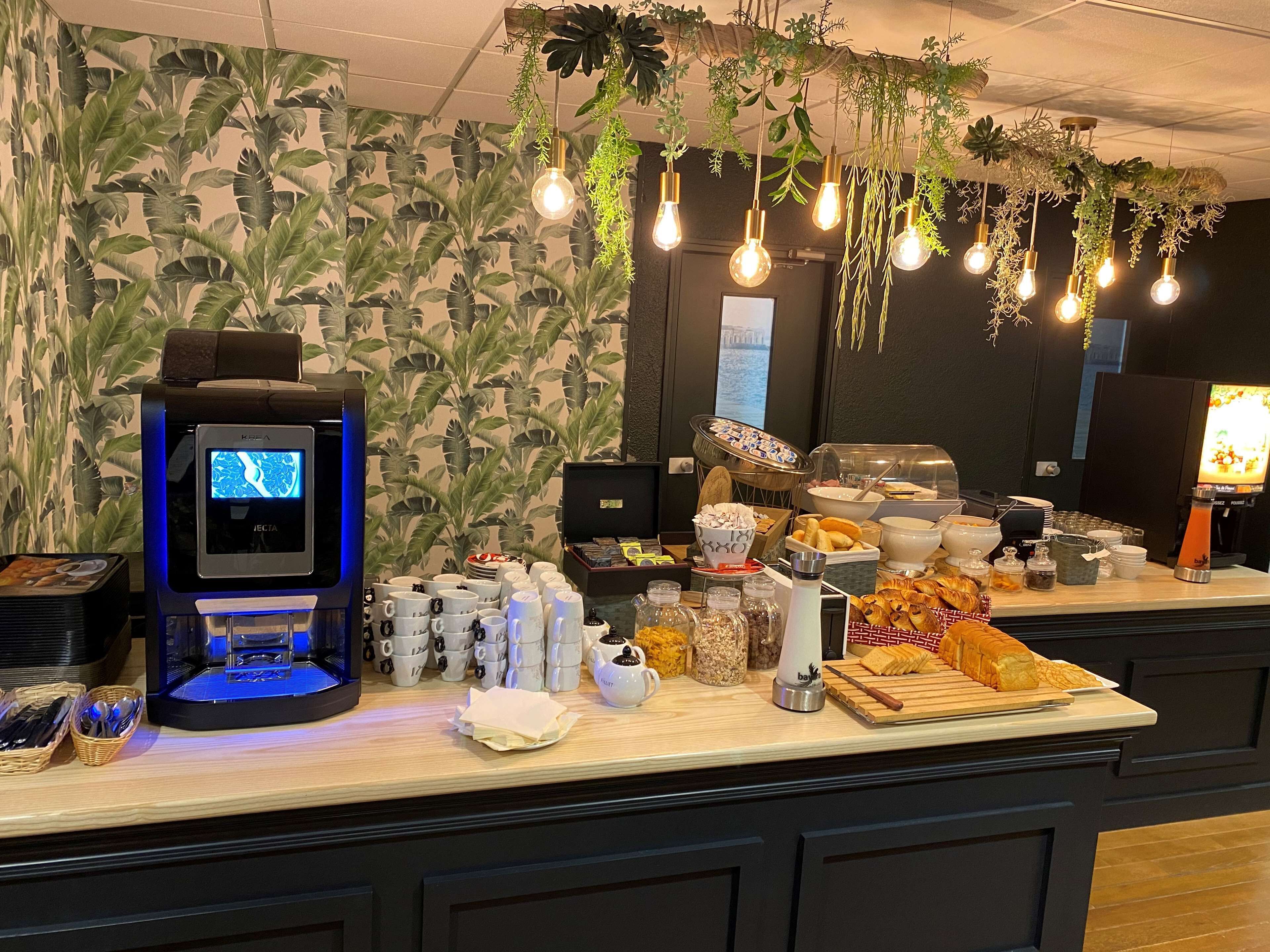 Un buffet avec une machine à café, divers plats et des plantes suspendues.