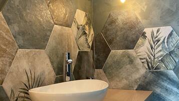 Un baño con un lavabo blanco tipo recipiente, una encimera de madera y baldosas de piedra hexagonales con diseños de hojas.