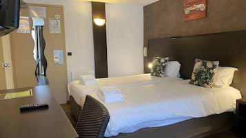 Habitación de hotel con dos camas, un escritorio y una silla. Se observa una lámpara fijada a la pared y un cuadro con la imagen de un coche.