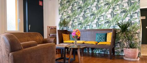 Un hall con un sofá marrón, una mesa de madera con un florero y una planta grande.