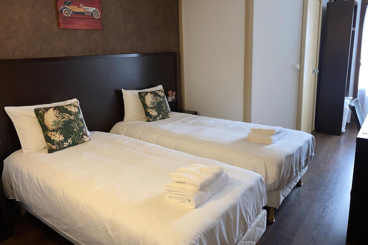 Ein Hotelzimmer mit zwei Betten, jedes mit weißer Bettwäsche und einem gefalteten Handtuch. Über den Betten befindet sich ein rotes Schild, und rechts eine Tür.
