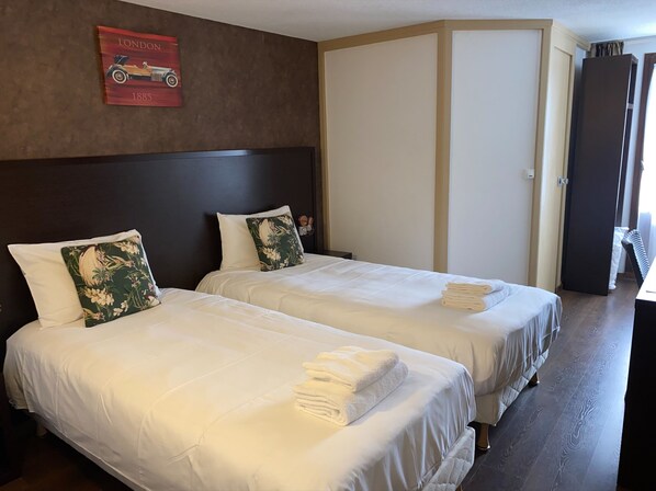 Habitación de hotel con dos camas, cada una con ropa blanca y una toalla doblada al lado. Hay un cartel rojo en la pared sobre las camas, y una puerta a la derecha.