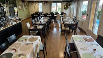 Restaurante com várias mesas preparadas para os clientes, área de bar com diversas bebidas, e janelas amplas que oferecem vista para o exterior.