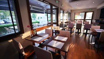 A restaurant with multiple tables and chairs, large windows with a view of the street, and a modern interior design.