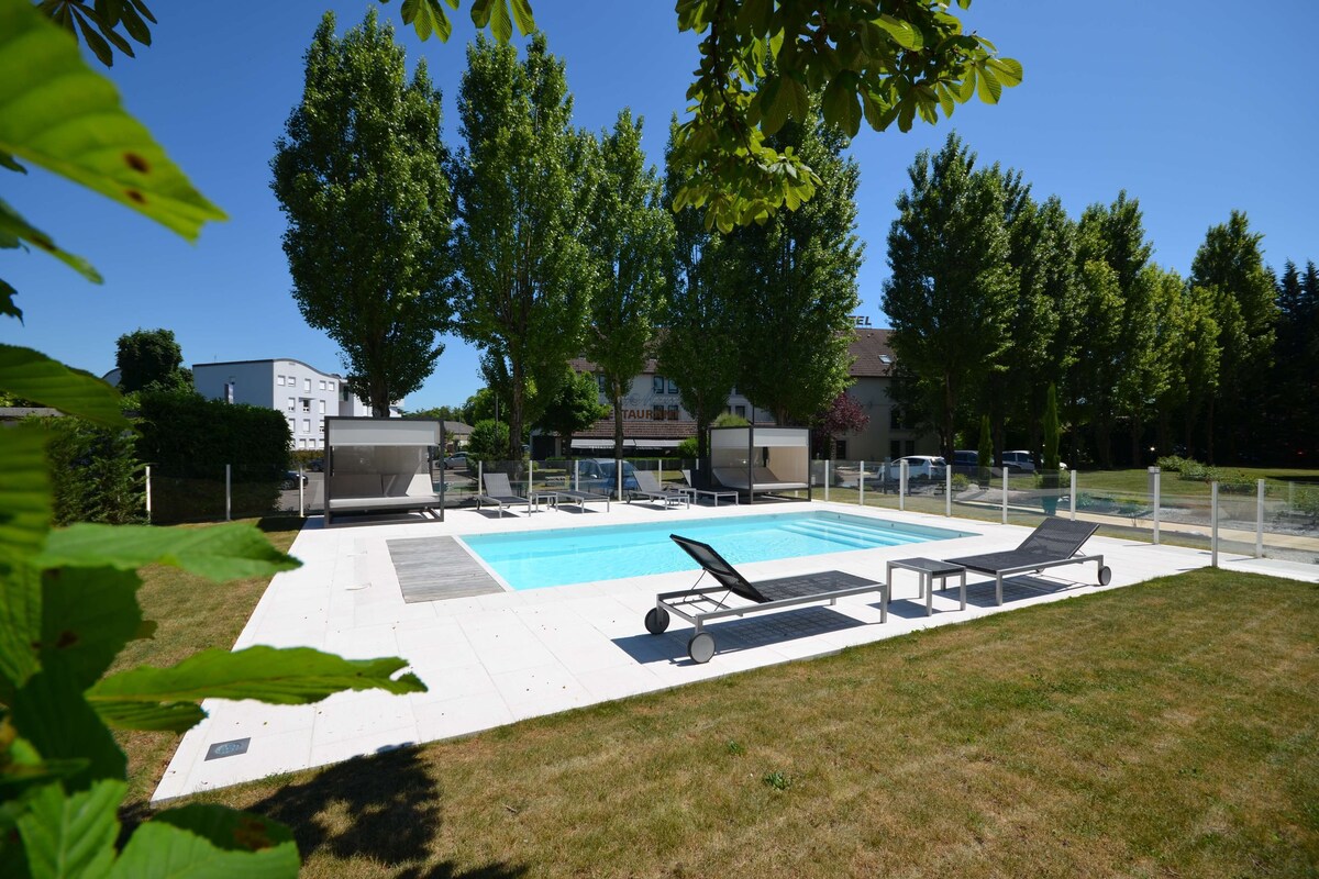 A swimming pool with lounge chairs, surrounded by trees and buildings.