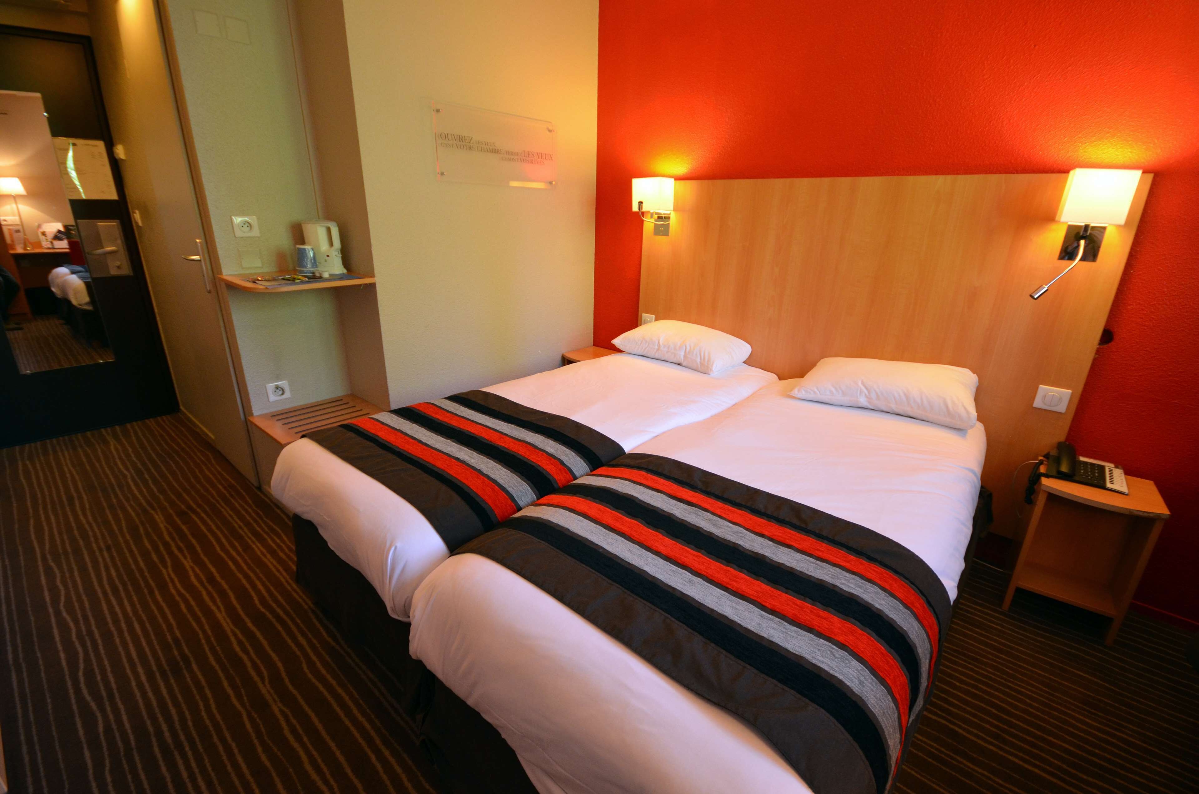 Camera d'albergo con un letto grande, due comodini, un tavolino e uno specchio, con una parete di colore rosso.