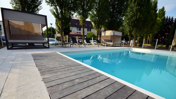 Una piscina con muelle de madera, sillas de descanso y un restaurante al fondo.