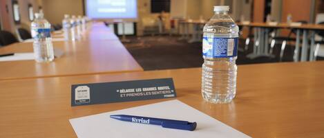 Un salón de conferencias con una larga mesa, botellas de agua, una tarjeta de identificación y un bolígrafo.