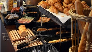 Un bufé con diversos alimentos, incluyendo pan y pasteles, dispuesto en un mostrador con cestas y utensilios de servicio.