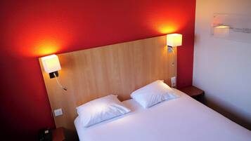 A hotel room with a wooden headboard, two white pillows, and bedside lamps.