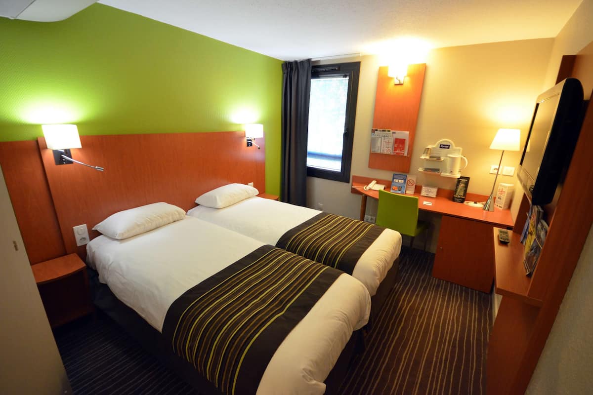 A hotel room with two beds, a desk with a telephone, a mirror, and a window with curtains.