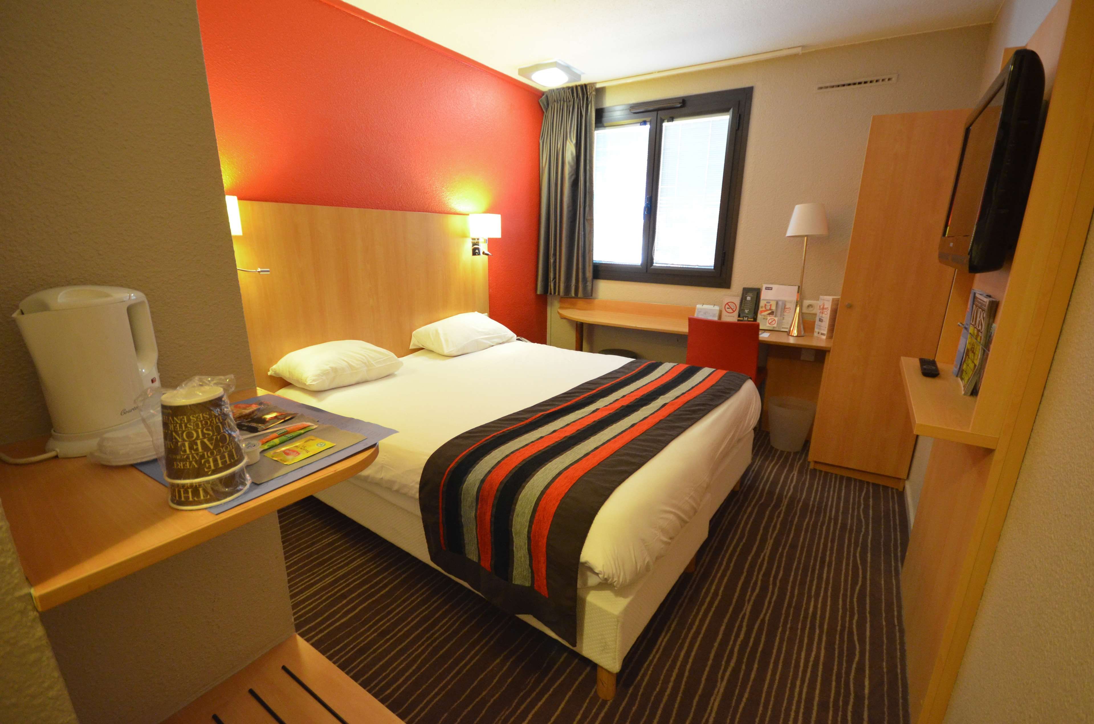 A hotel room with a bed, bedside table, lamp, and a window with curtains.